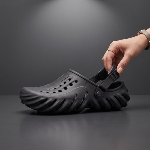 Sabot Echo Clog noir LAS ROSAS en mousse sculptée avec bride ajustable, tenu à la main sur fond gris studio.